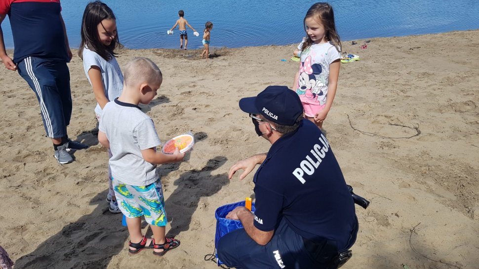 Na plaży nad Łysiną policjant wręcza dzieciom upominki