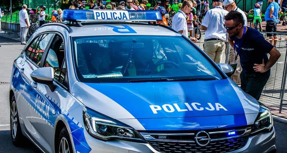 Policyjny radiowóz na zabezpieczeniu wyścigu, przy kierowcy nachyla się mężczyzna