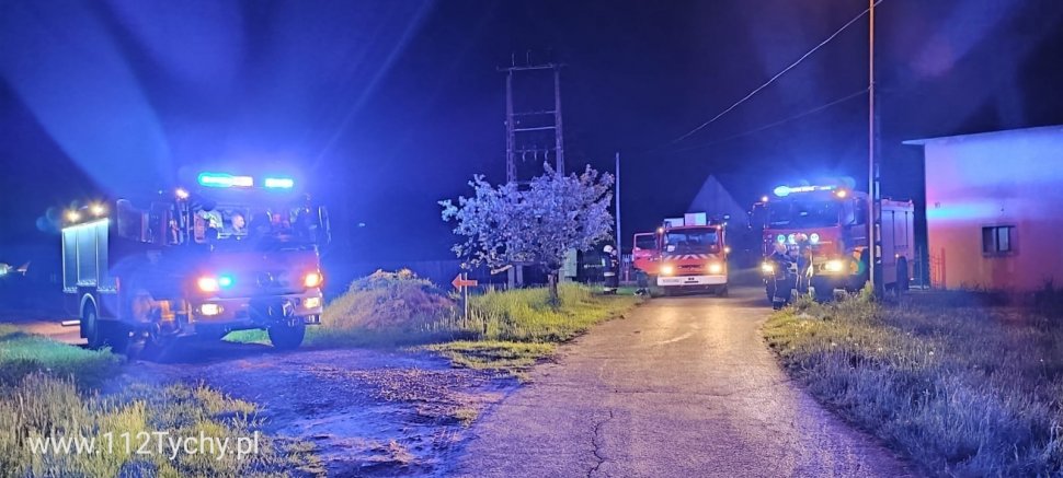 Wozy strażackie z włączoną sygnalizacją świetlną stoją przy drodze. Zdjęcie wykonane w porze nocnej