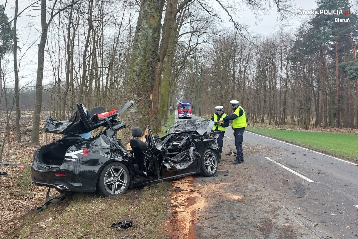 Na zdjęciu widzimy uszkodzone auto w wyniku wypadku drogowego oraz policjantów w czasie wykonywania czynności na miejscu zdarzenia drogowego