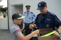 Policjant wręcza dziecku odblask, w tle strażnik miejski