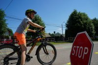 W lewej części zdjęcia chłopiec na rowerze w trakcie egzaminu na kartę rowerową, po prawej stronie czerwony znak STOP stoi na boisku