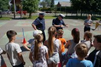 Na pierwszym planie stoją dzieci, na drugim planie policjanci i nauczycielka