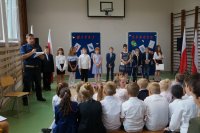 Policjant i uczniowie na sali gimnastycznej podczas uroczystego apelu z okazji rozpoczęcia roku szkolnego