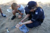 Policjantka i chłopiec kucają na piasku. Policjantka trzyma gadżety z napisem &quot;Kręci mnie bezpieczeństwo nad wodą&quot;