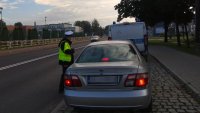 Policjant zaparkowanego przy jezdni samochodu kontroluje kierowcę
