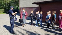 Policjant i nauczycielka stoją z grupą dzieci przy szkole