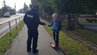 Policjant przy szkole wręcza odblask chłopcu na hulajnodze