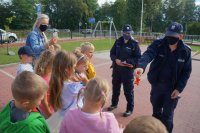 Policjanci przeprowadzają pogadankę z grupą dzieci, policjant trzyma w ręku odblask
