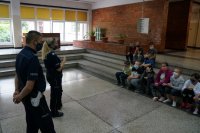 Na szkolnej auli policjanci prowadzą prelekcję, dzieci siedzą na schodach