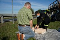 Działania Road Safety Days na DK44 w Bieruniu, strażak demonstruje na fantomie udzielanie pierwszej pomocy przedmedycznej, na pierwszym planie widać klęczącego mężczyznę