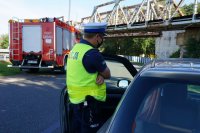 Działania Road Safety Days na DK44 w Bieruniu, policjant stoi przy zatrzymanym do kontroli drogowej samochodzie, w tle stoi wóz strażacki