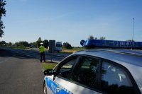 Działania Road Safety Days na DK44 w Bieruniu, na pierszym planie widać fragment radiowozu, w tle stoi policjant i obserwuje jezdnię