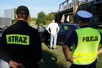 Działania Road Safety Days na DK44 w Bieruniu, na pierwszym planie stoją tyłem strażak i policjant, w tle strażak udziela instruktażu mężczyźnie w białej koszulce