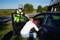 Działania Road Safety Days na DK44 w Bieruniu, mężczyzna w białej koszulce wyciąga z pojazdu manekina, policjant stoi oparty o drzwi pojazdu i przygląda się