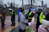 Policjanci wręczają odblaski mieszkańcom. W tle widać wozy strażackie.