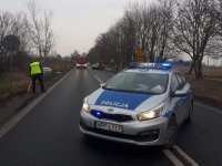 Policjant pracuje na miejscu wypadku. Na pierwszym planie, w poprzek jezdni stoi radiowóz