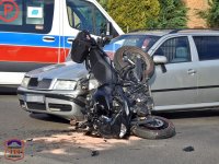 Samochód osobowy i motocykl, które zderzyły sie na drodze. Na drugim planie stoi karetka pogotowia.