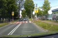 Zdjęcie kolorowe - kadr nagranej przez kamerę samochodową sytuacji na przejściu dla pieszych. Na zdjęciu widać oznakowane przejście dla pieszych, po prawej stronie dwóch chłopców, którzy odskakują na chodnik. Przed przejściem stoi jeden samochód, a drugi wykonuje manewr omijania go bezpośrednio przed pasami.