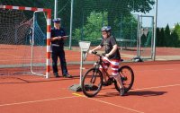 Na szkolnym boisku policjant ruchu drogowego stoi przy bramce, uczeń zdaje egzamin - jedzie na rowerze po wyznaczonej drodze