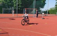 Na boisku szkolnym policjant ruchu drogowego stoi przy bramce. Uczeń zdaje egzamin - jedzie na rowerze po wyznaczonej drodze