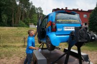 Mężczyzna w błękitnej koszulce zamyka drzwi symulatora dachowania - pojazdu w kolorze błękitnym