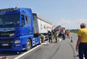 Miejsce wypadku drogowego, tir uczestniczący w wypadku stoi na poboczu, służby wykonują czynności. Na jezdni widać ślady hamowania