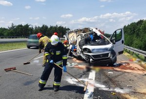 Miejsce wypadku drogowego, rozbity samochód stoi na jezdni, Strażacy sprzątają jezdnię