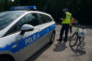 Przy radiowozie stoi policjanti osoba kontrolowana a obok rower