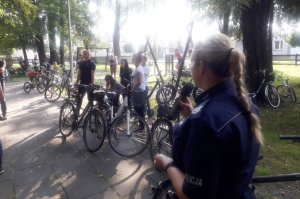 Policjantka w Parku Dworskim rozmawia z uczestnikami imprezy plenerowej, którzy stoją przy rowerach