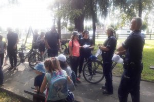 Policjanci w Parku Dworskim rozmawiają z uczestnikami imprezy plenerowej, którzy stoją z rowerami