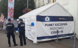 Policjant i strażnik miejski stoją przy białym namiocie - mobilnym punkcie szczepień przeciwko Covid-19