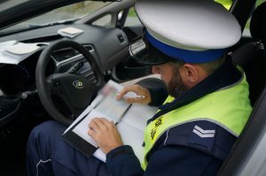 POlicjant ruchu drogowego w odblaskowej kamizelce siedzi w radiowozie i sporządza dokumentację z kontroli drogowej