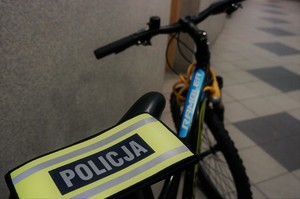 Odzyskany przez poilicjantów rower stoi w korytarzu bieruńskiej komendy. Na pierwszym planie widać opaskę odblaskową z napisem POLICJA