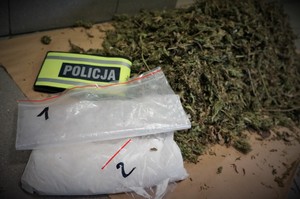 Zabezpieczone przez policjantów substancje zabronione leżą na kartonie wraz z odblaskową opaską , na której jest napis POLICJA