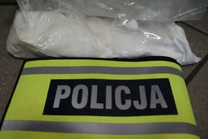 W górnej części zdjęcia widać foliowy worek z białą substancją, poniżej znajduje się odblaskowa opaska z napisem POLICJA