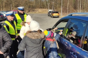 Policjanci i dzieci stoją przy granatowym samochodzie. W tle widać parking