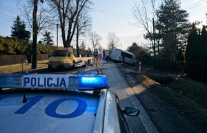 Miejsce wypadku. Na pierwszym planie radiowóz z włączoną sygnalizacją świetlną. Na drugim planie jezdnia, samochód pomocy drogowej i dwa pojazdy w przydrożnym rowie