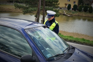 Na pierwszym planie samochód, na drugim planie przy kierowcy stoi policjant ruchu drogowego