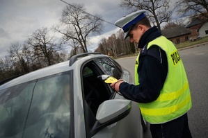 Policjant ruchu drogowego stoi przy zatrzymanym do kontroli samochodzie. Trzyma w dłoni urządzenie do pomiaru trzeźwości