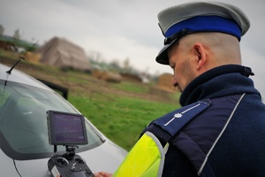 Na pierwszym planie przy monitorze stoi policjant ruchu drogowego obsługujący drona.