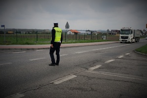 Na jezdni tyłem stoi policjant ruchu drogowego w zielonej odblaskowej kamizelce