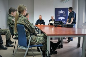 Sakla odpraw bieruńskiej komendy. Przy dużym stole konferencyjnym, na pierwszym planie siedzą uczniowie z klasy mundurowej. Na drugim planie widać troje policjantów, którzy prowadzą zajęcia z uczniami