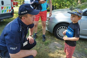 Komendant Powiatowy Policji w Bieruniu kuca przed małym chłopcem trzymającym odblask. W tle widać zaparkowany samochód w kolorze srebrnym
