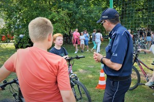 Na boisku Mini Arboretum po prawej stronie stoi policjant, a przed nim po lewej stronie stoją chłopcy z rowerami