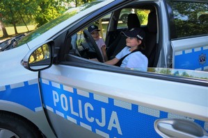 W policyjnym radiowozie siedzą dwie dziewczynki. W dolnej części zdjęcia na drzwiach pojazdu widać napis POLICJA