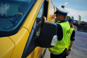 Dwoje policjantów w trakcie kontroli drogowej stoi przy oknie kierowcy żółtego samochodu