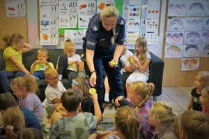 Policjantka wręcza zawieszki odblaskowe dzieciom siedzącym na podłodze i kanapie