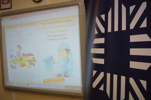 Zbliżenie na ekran rzutnika, na którym widać animowaną prezentację na temat bezpieczeństwa nad wodą. W prawej części zdjęcia policyjna gwiazda na granatowym tle