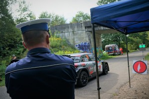 Na zdjęciu widać miejsce startowe. Na pierwszym planie stoi policjant ruchu drogowego w czapce z białym otokiem, przygląda się samochodowi oczekującemu na start. W tle widać karetkę pogotowia zaparkowaną przy poboczu jezdni.